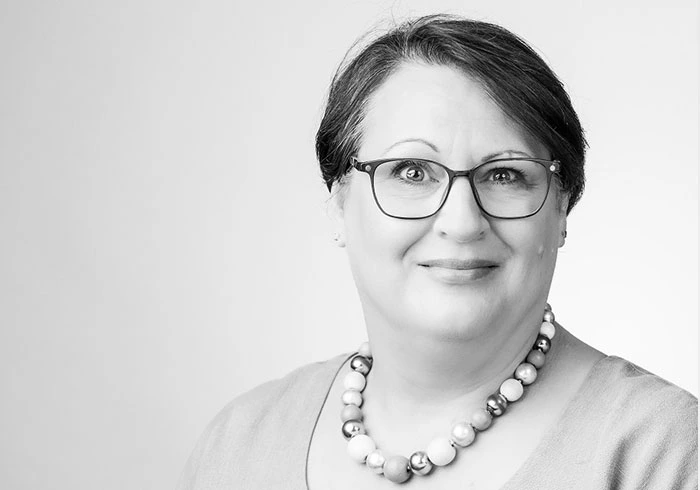 Sie hat kurzes, dunkles Haar trägt eine Brille und grinst freundlich in die Kamera.