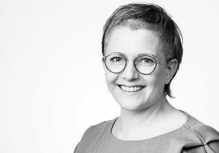 Sie hat kurzes Haar, trägt eine Brille und lacht freundlich in die Kamera.