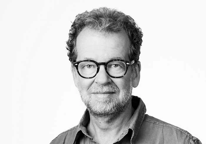 Mann mit Brille, Bart und lockigem Haar schaut freundlich in die Kamera.