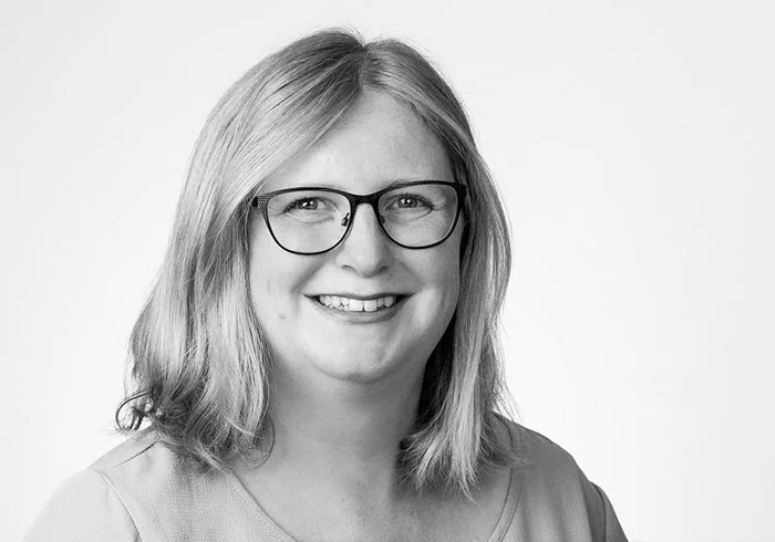 Sie hat schulterlange, glatte Haare, trägt eine Brille und lacht freundlich in die Kamera.