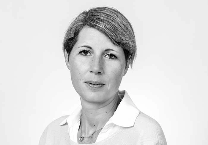 Frau mit kurzem Haar und neutralem Ausdruck blickt in die Kamera.