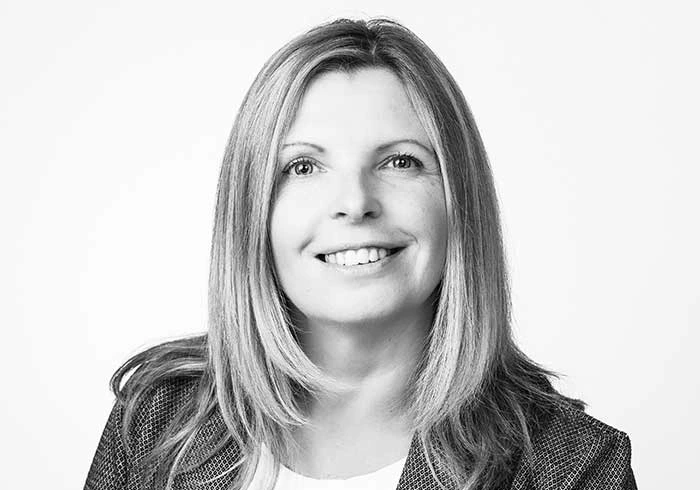 Lächelnde Frau mit mittellangen Haaren und kariertem Blazer.