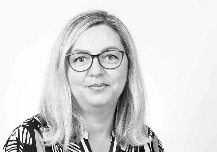 Frau mit Brille und langen Haaren lächelt freundlich in die Kamera.