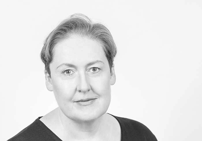 Frau mit kurzem Haar und ruhigem Gesichtsausdruck, direkter Blick.