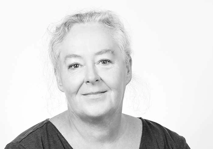 Frau mit lockigem Haar und sanftem Lächeln blickt freundlich in die Kamera.