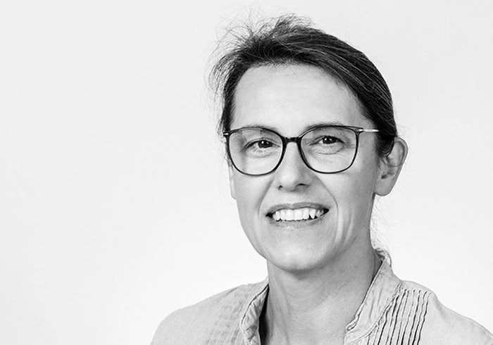 Sie hat glatte, dunkle Haare, trägt eine Brille und lacht in die Kamera.