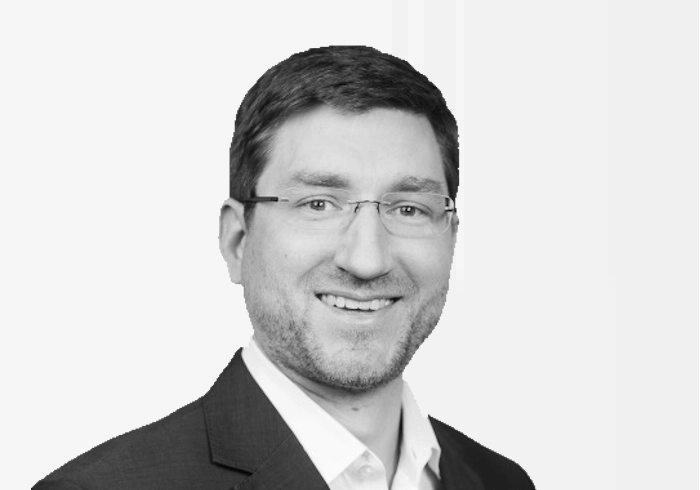 Mann mit Brille und Sakko schaut ruhig und direkt in die Kamera.