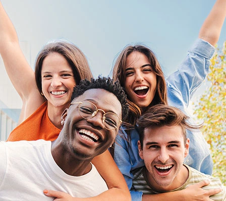 Vier junge Menschen lachen und posieren fröhlich im Freien bei sonnigem Wetter.